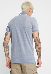 Grå polo t-shirt med korte ærmer, der har kontrastfarvet krave og manchetter. Blød tekstur med sideslids for let bevægelse.