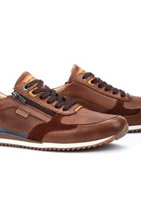 Sneakers in pelle marrone con accenti in rete, punta rotonda, dettagli gialli a contrasto, chiusure con zip e superfici testurizzate su una suola bianca.