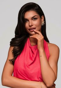 Haut sans manches drapé rose avec une texture douce, porté avec des boucles d'oreilles en forme de fleur ; modèle avec des cheveux foncés et un bracelet discret au poignet.