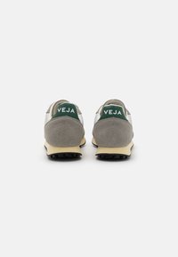 Grå semsket lær og mesh sneakers med grønne hælklapper, der har "VEJA" i hvid tekst og beige gummisåler. Teksturdesign med sporty look.