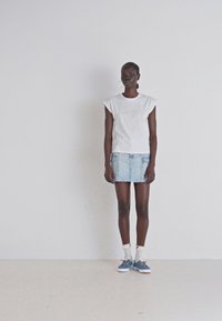 Hvid kortærmet T-shirt, blå denim mini-skirt og blå sneakers med hvide snørebånd. Har et afslappet design og minimale detaljer.