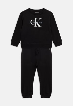 Sort langærmet sweatshirt og bukser med Calvin Klein-logo i hvidt og gråt på brystet, elastiske manchetter og snøre i taljen.