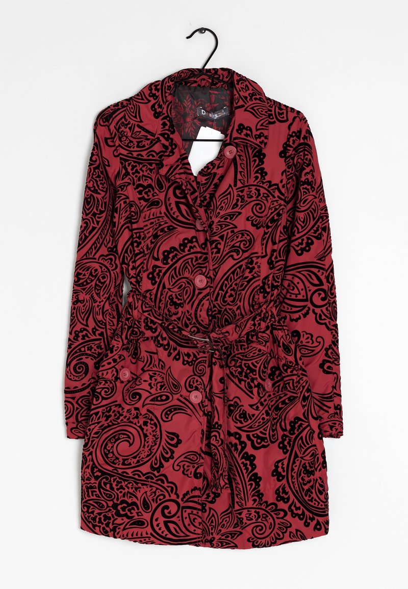 Rood ceintuurcoat met zwarte paisleypatronen, met knopen aan de voorkant, lange mouwen en twee klepzakken, hangend aan een zwarte hanger.