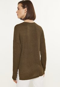 Olivgrüner gerippter Pullover mit langen Ärmeln, rundem Halsausschnitt und seitlichen Schlitzen. Weiche Textur mit dezentem Glanz, entworfen für eine lockere Passform.