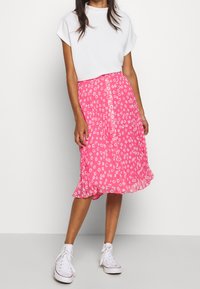 Jupe midi florale rose avec un ourlet évasé, ornée de fleurs blanches et de boutons devant. Associée à un t-shirt blanc simple et des baskets.