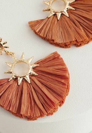 Orecchini in rafia color terracotta, con un accento a forma di sole in tonalità oro testurizzata. Le ventole sono sovrapposte con dettagli di frange delicate.