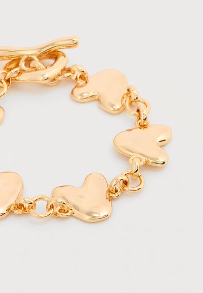 Βραχιόλι σε χρυσαφί τόνο με γυαλιστερές ακανόνιστες καρδιές συνδεδεμένες με στρογγυλούς κρίκους και κούμπωμα τύπου τογκλ σε λευκό φόντο.