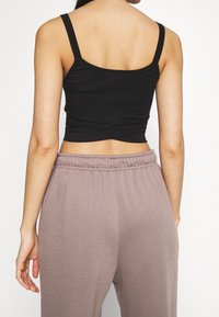 Czarny krótki top na ramiączkach, wykonany z gładkiego materiału. Połączony z jasnofioletowymi spodniami dresowymi z elastycznym pasem, ukazującymi strukturę.