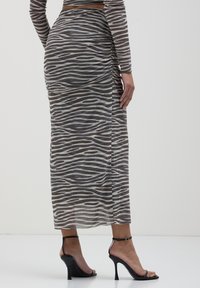 Gonna maxi con stampa zebra grigia e beige, realizzata in tessuto trasparente con dettagli arricciati lungo il lato, abbinata a tacchi a spillo neri.