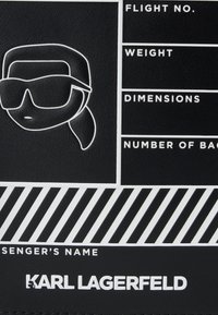 Stylizowana twarz w okularach przeciwsłonecznych i kucyku obok pustych pól dotyczących lotu, wagi, wymiarów i bagażu na czarnym tle z logo Karla Lagerfelda.