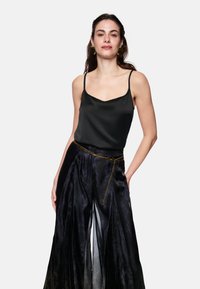 Black satin camisole with thin straps paired with a black, pleated skirt featuring a gradient pattern and a gold chain belt.