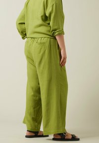Groene linnen wijde pijpen broek met een comfortabele elastische tailleband, zakken en een ontspannen pasvorm, gecombineerd met zwarte platte sandalen.