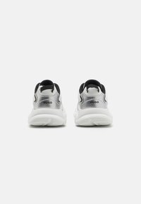 Zapatillas blancas con parte superior de malla y acentos plateados, detalles negros en el talón y una suela blanca texturizada para mayor agarre.