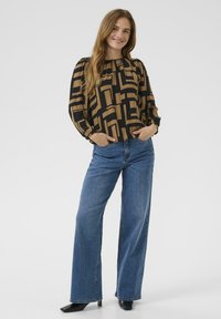 Long-sleeve black and brown patterned blouse with gathered neckline, paired with wide-leg blue jeans and black pointed-toe heels.