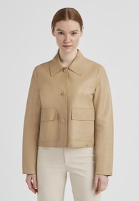Beige Leder-Cropped-Jacke mit breitem Kragen, vorderem Knopfverschluss und zwei aufgesetzten Taschen. Glatte Textur und minimale Hardware-Akzente.