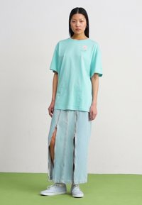 Tricou din bumbac bleu deschis cu un mic logo, asortat cu o fustă lungă din denim deschis, cu slituri laterale și tiv brut. Puratat cu adidași bleu deschis.