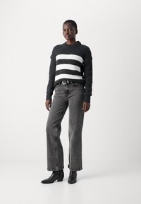 Svart-hvitt stripete strikkegenser med ribbestruktur, matchet med høyt liv grå jeans og svarte spisse støvler.