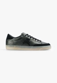 Zapatilla negra de corte bajo con acabado brillante, cordones negros, logotipo de calavera y huesos cruzados en el lateral, y suela texturizada translúcida.