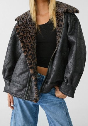 Woman wearing a black textured leather jacket with leopard print faux fur collar, paired with a black crop top and blue jeans.