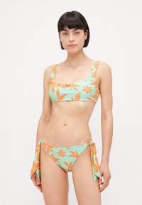 Svjetloplavi bikini set s odvažnim narančastim cvjetnim uzorcima, top s četvrtastim izrezom i podesivim naramenicama te gaćice s vezanjem sa strane.