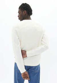 Gaišs kr�ēma krāsas džemperis ar vienkāršu dizainu, ribotiem piedurkņu galiem un teksturētu aizmugures daļu. Apvienots ar ziliem džinsiem, kas izceļ brīvu piegulšanu.