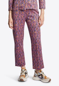 Spodnie w kolorowe wzory z geometrycznym motywem w odcieniach różu, fioletu i pomarańczy. Noszone z białymi i pomarańczowymi trampkami.