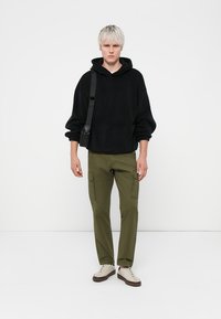 Zwarte fleece hoodie met een kangoeroezak, gecombineerd met olijfgroene cargobroek met zijzakken. Beige sneakers maken de look af.