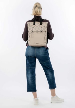 Mochila geométrica beige con patrón triangular negro, correas ajustables negras y un bolsillo delantero con cremallera. Material ligero y duradero.
