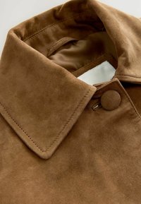 Collo in camoscio marrone con chiusura a bottone e una fodera interna liscia. Presenta un design del collo a punta e una cucitura sottile.