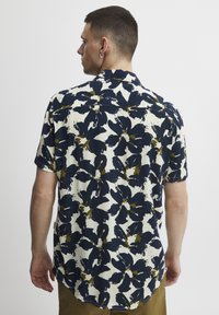 Camisa de manga corta en color crema con estampado floral abstracto en azul marino y oliva, con un corte relajado, botones y dobladillo curvo.