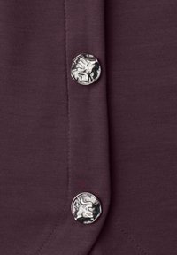 Deux boutons ronds et irréguliers en argent sur un tissu violet foncé avec des coutures visibles le long de la couture centrale.