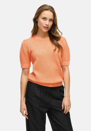 Pull en tricot texturé pêche avec des manches courtes bouffantes et un ourlet côtelé, associé à un pantalon noir plissé. Les deux pièces sont ajustées.