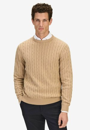 Beige kabelgebreide trui met een ronde hals, geribde manchetten en zoom. Draagt over een witte overhemd met kraag, met een gestructureerd oppervlak.
