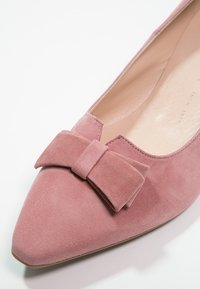 Scarpa piatta in suede rosa con punta appuntita e un'accattivante fascia sul collo del piede; fodera interna liscia e design minimalista.