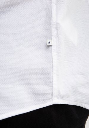 Biała koszula z krótkim rękawem, wykonana z teksturowanego materiału siateczkowego. Posiada czarny dolny brzeg i małą naszywaną metkę z gwiazdką.