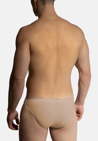 Světle béžové pánské slipy s hladkým povrchem, elastickým pasem a minimálním pokrytím, zobrazené zezadu na jednoduchém pozadí.