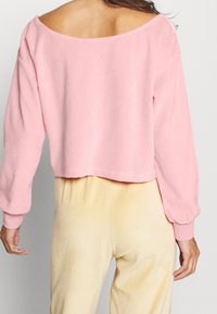 Sweat-shirt rose court avec large encolure, manches longues et texture douce ; associé à un pantalon moelleux jaune clair.