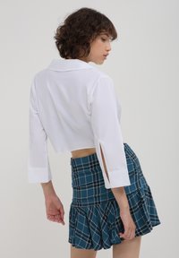 Blusa bianca corta con maniche 3/4 e fessure laterali abbinata a una mini gonna a quadri blu con orlo arricciato e vita elastica.