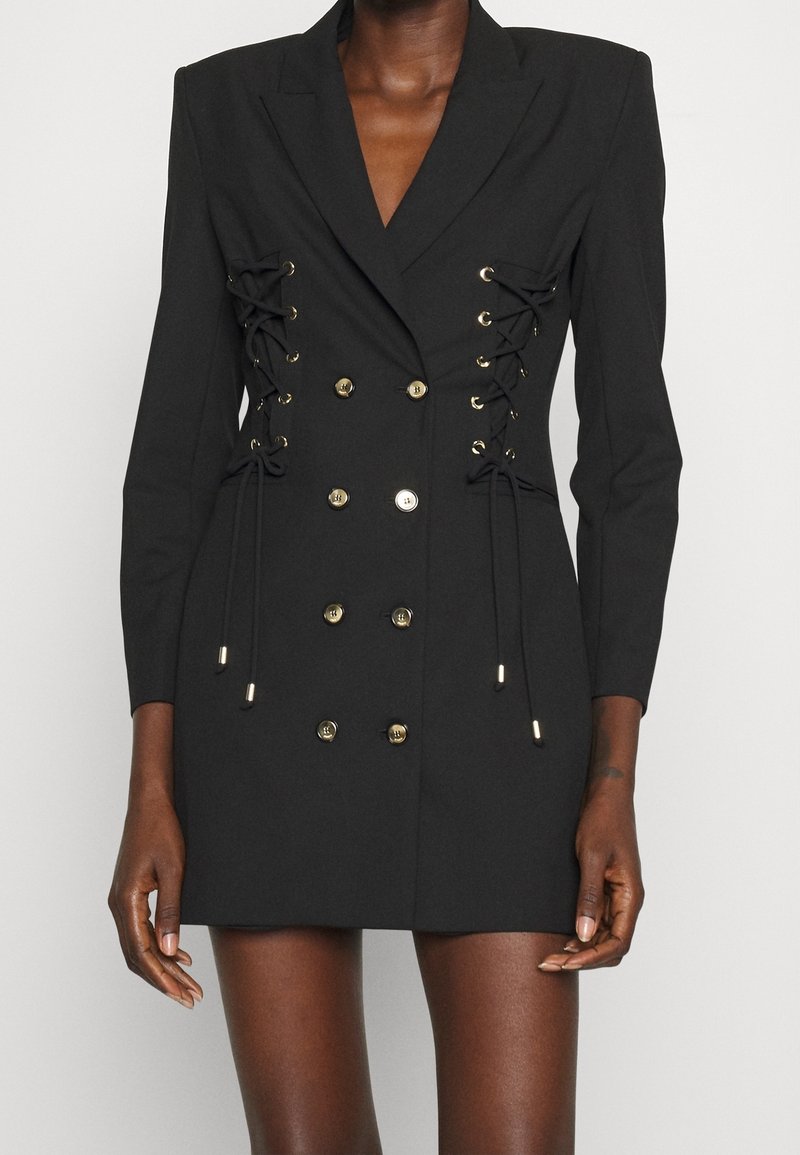 Robe blazer noire à double boutonnage, ornée de détails en métal doré, avec des lacets sur les côtés et des manches longues.