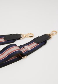 Il cinturino presenta un tessuto intrecciato a righe blu navy, rosa e crema, con dettagli in pelle nera e clip in metallo color oro. Etichetta del marchio visibile.