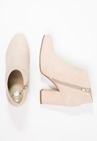 Botas de tobillo beige con una textura suave de ante, que cuentan con una cremallera lateral y un tacón cuadrado. Diseño de punta afilada.