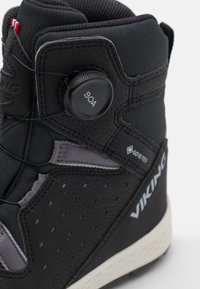 Botte noire imperméable avec une tige synthétique texturée, un accent gris et un système de réglage BOA avec une semelle extérieure blanche.