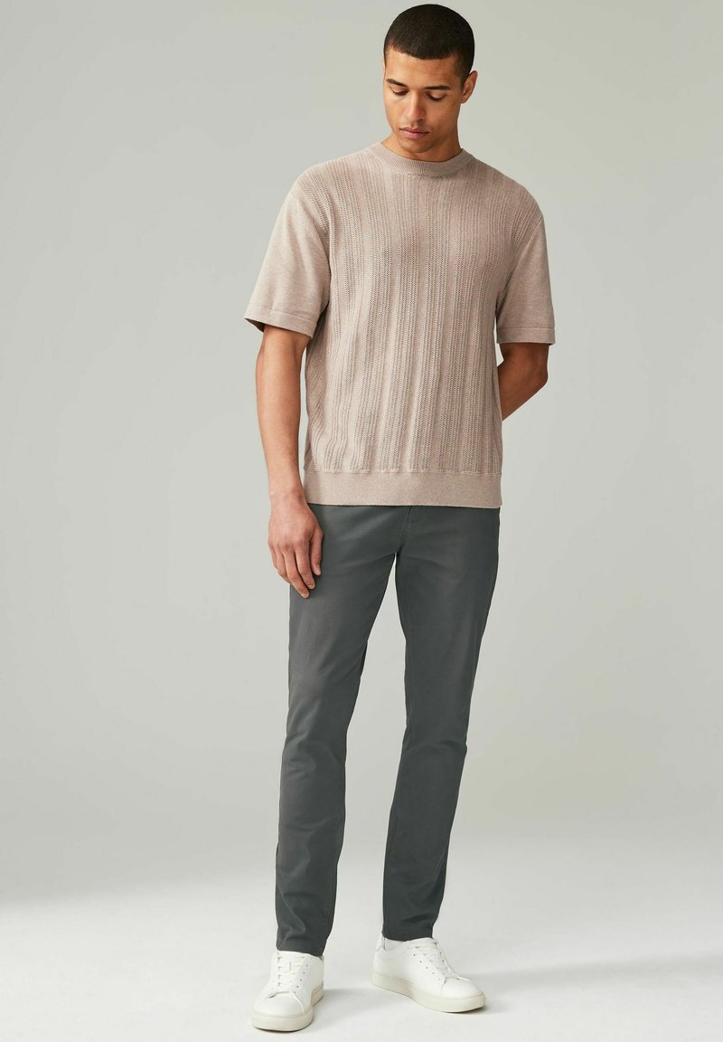 Pull en tricot beige à côtes et à manches courtes associé à un pantalon slim gris foncé et des baskets blanches. Design simple, coupe décontractée, tissu texturé.