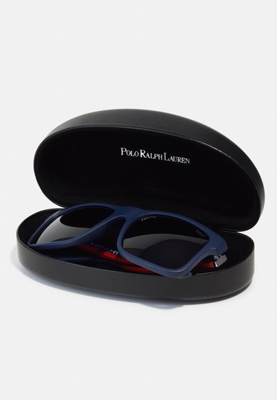 Occhiali da sole blu navy con lenti scure, custoditi in una custodia ovale nera con un logo. La custodia ha una superficie liscia e una lucentezza sottile.