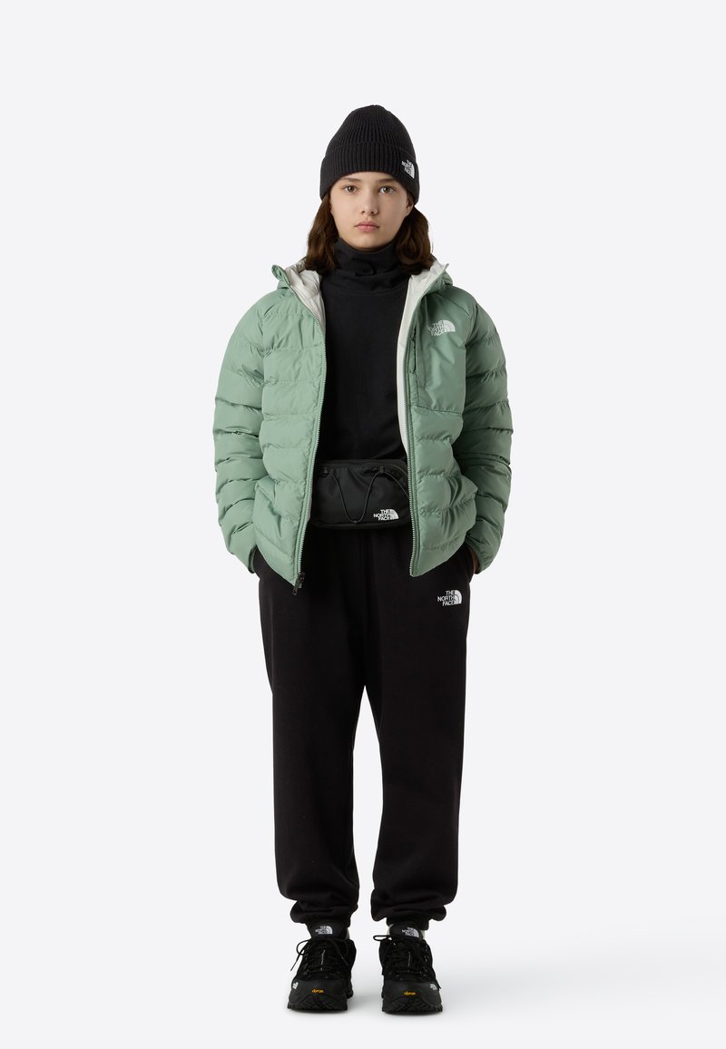 Padjandusega heleroheline jakk valge voodriga, must kõrgekaelusega kampsun, mustad vabaaja püksid ja mustad tossud. Omad logode aktsente ja lõdva istuvusega.