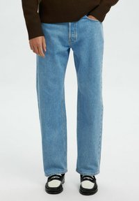 Gai zilas taisnas kājas džinsi ar izbalējušu apdari, valkāti ar melnām kurpēm ar baltu akcentu. Audums izskatās pēc džinsa un ir nedaudz teksturēts.