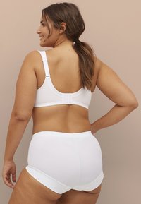 Weißer BH mit verstellbaren Trägern und Hakenverschluss, kombiniert mit weißen hochgeschnittenen Panties. Verfügt über glattes Material und minimale Nähte.