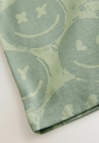 Katoenen t-shirt in gedempt groen met een herhalend patroon van glimlachende gezichten en x'en, met een ronde hals en gestikte zoomdetails.