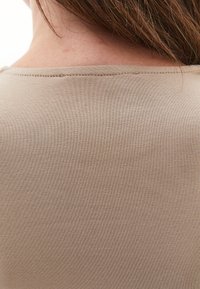 Lähikuva henkilön yläselästä ja niskasta, jossa on ruskeat hiukset ja päällä beige ribattu paita.