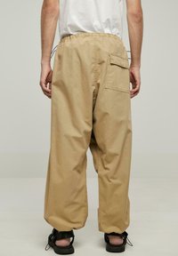 Beige, lette, bomuldsbukser med elastisk talje, sidelommer og en stor påsyet lomme bagpå. Afslappet pasform.
